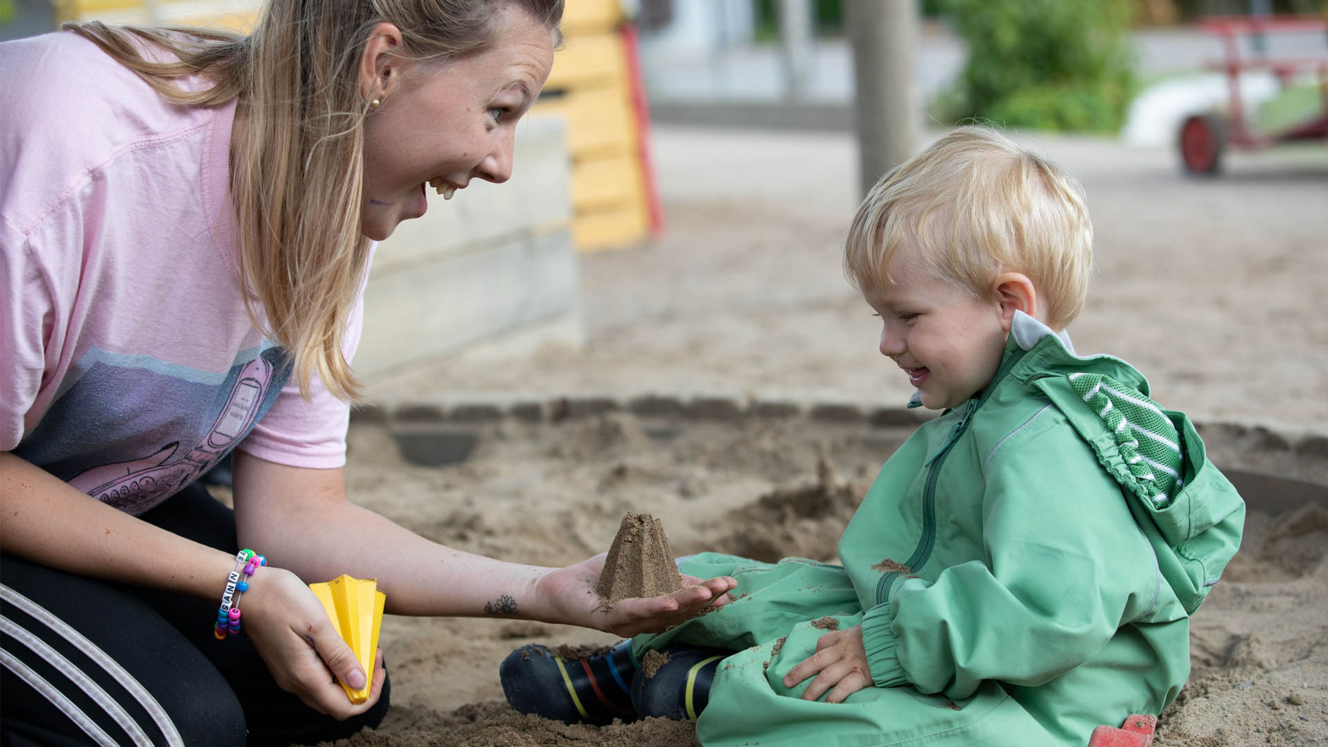 Barn och lärare leker i sandlådan, läraren visar sand som blivit formad för barnet