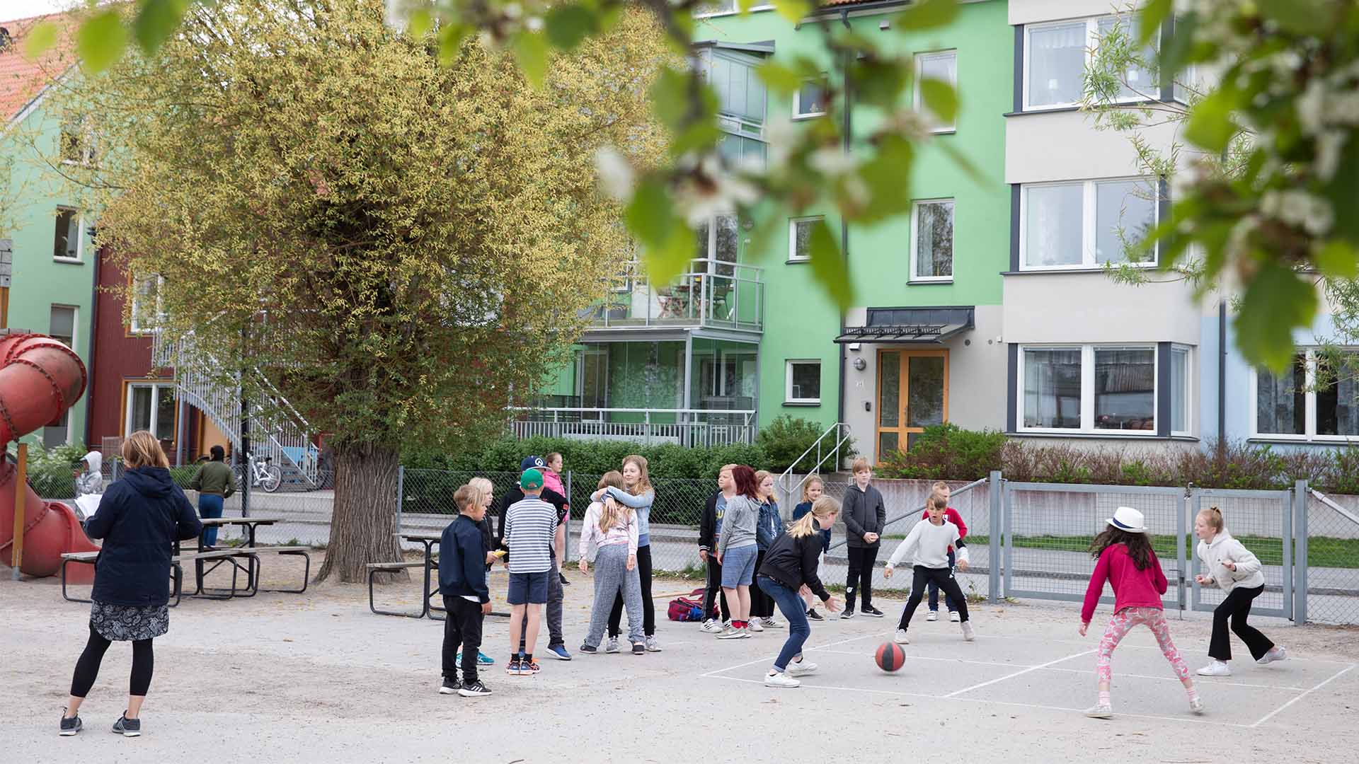 Flera barn befinner sig i en skolgård, några barn spelar med en boll på marken