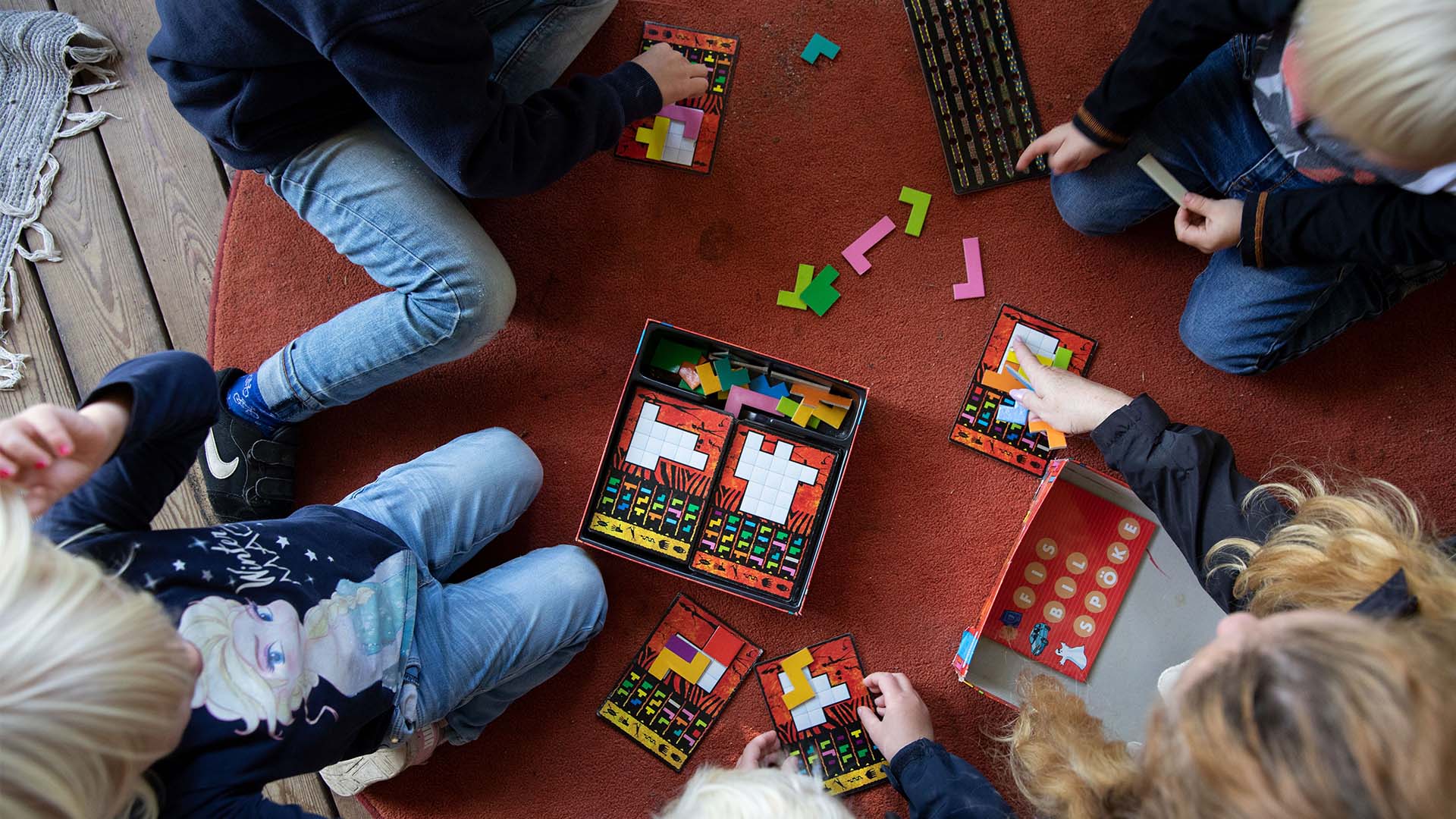 Fyra barn sitter ner vid en röd matta och lägger ut tetris-liknande av ett pussel