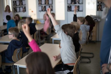 Barn i klassrum som räcker upp handen