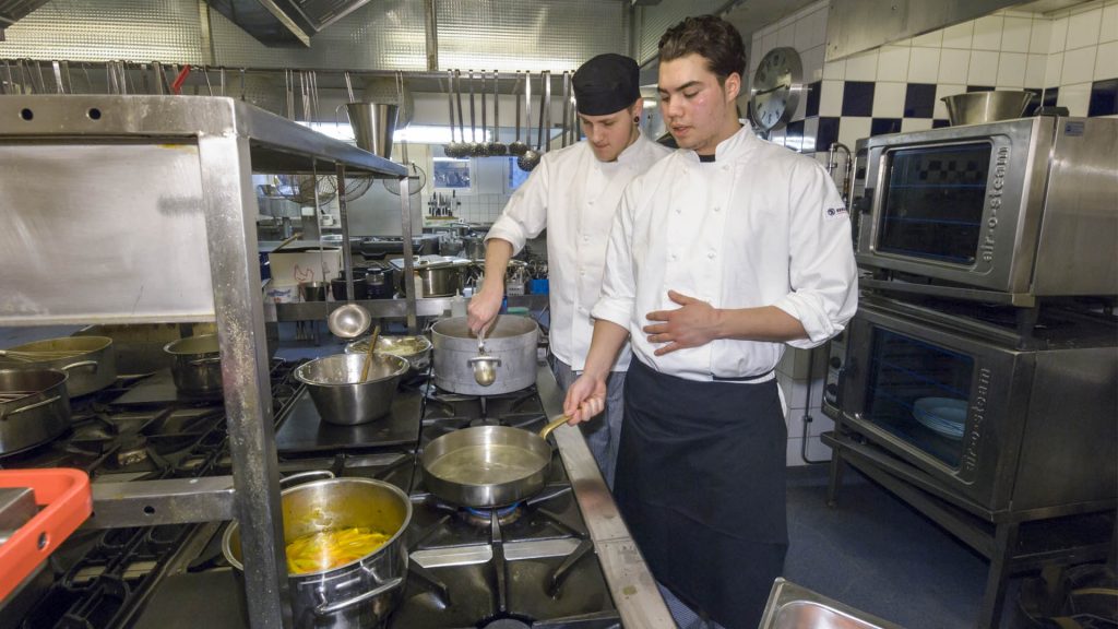 Två elever står i ett kök och lär sig om matlagning.