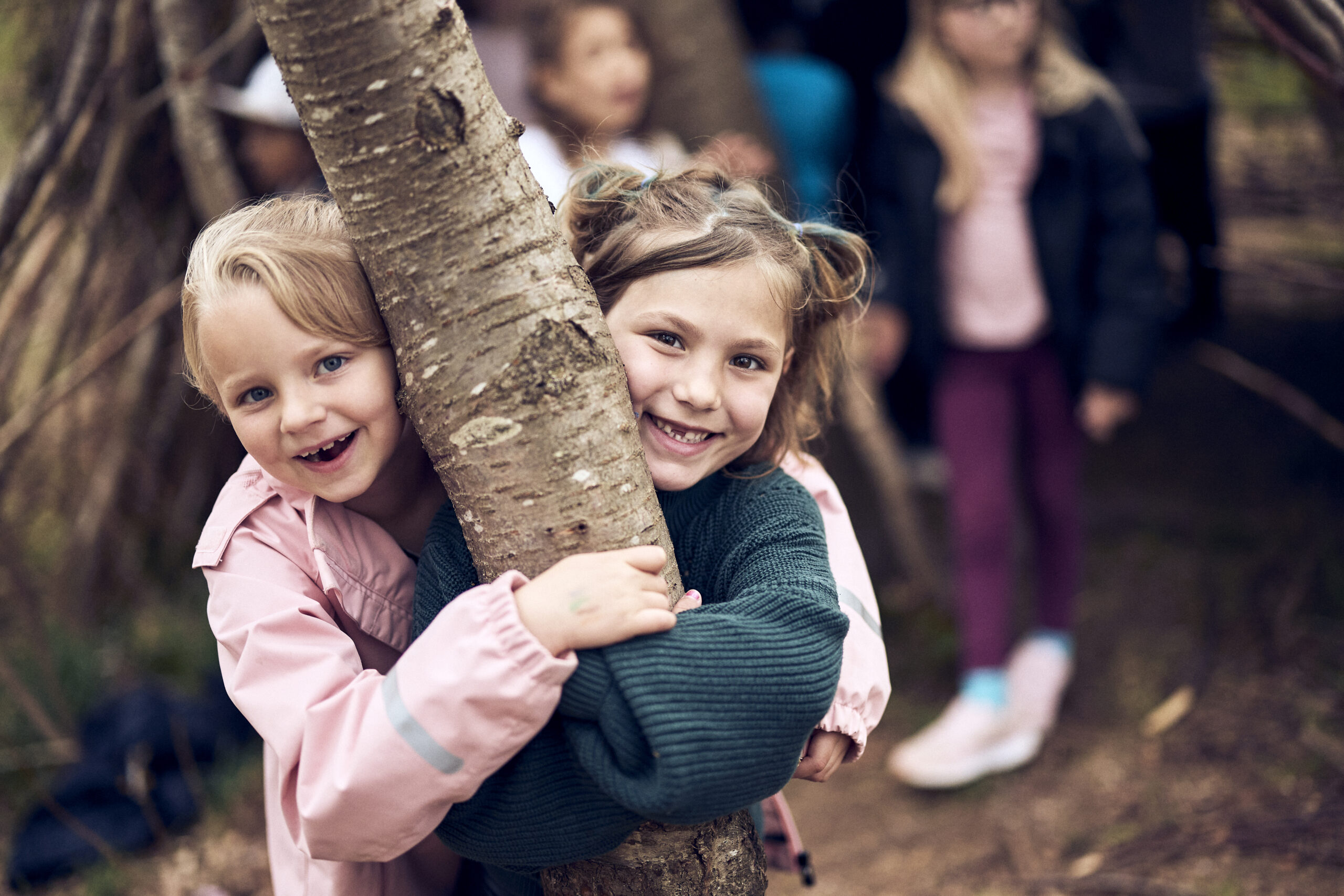 Två barn ler stort och kramar ett träd