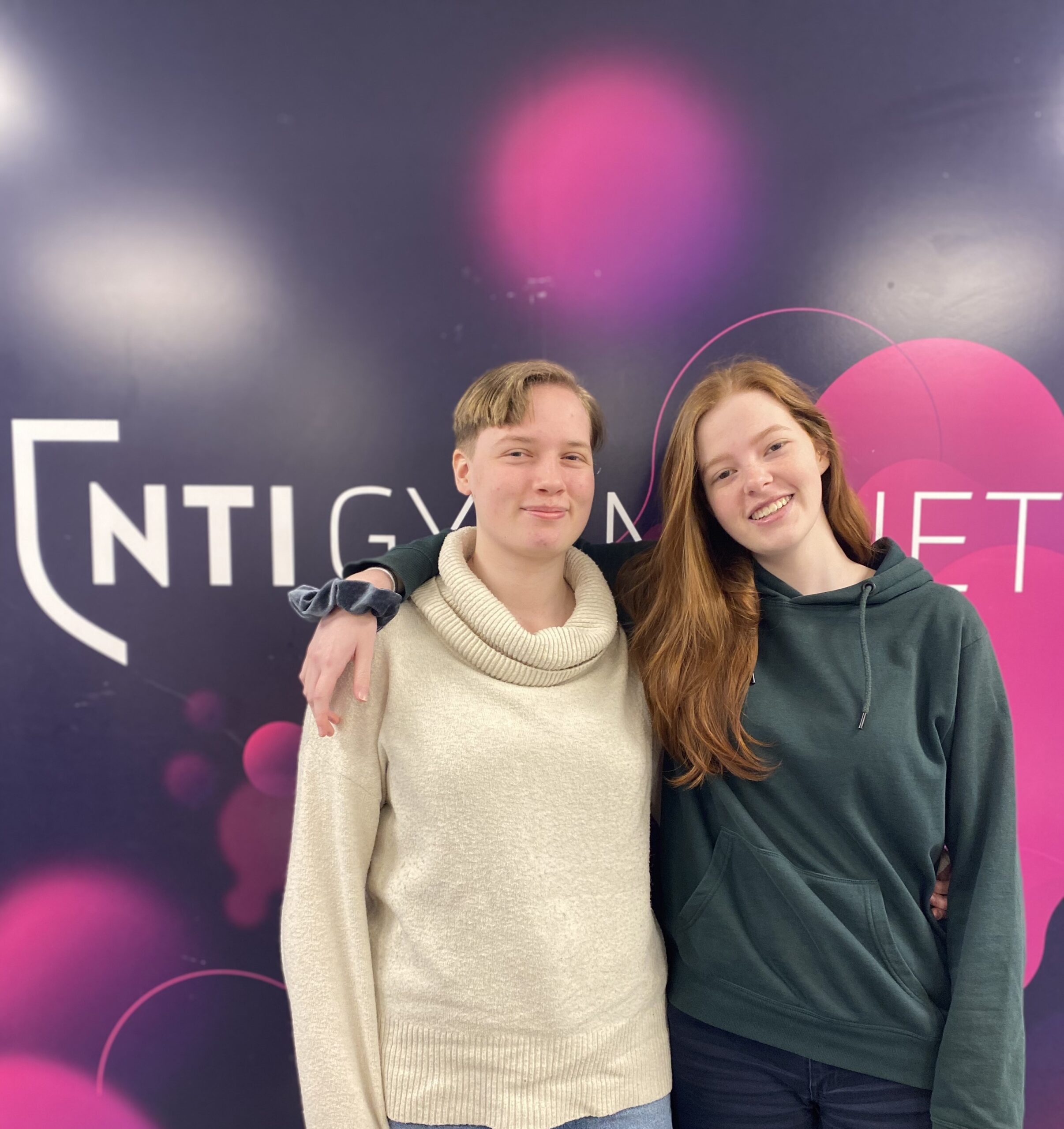 Alicia Källgren och Sara Svedberg står bredvid varandra framför en logga av NTI Gymnasiet